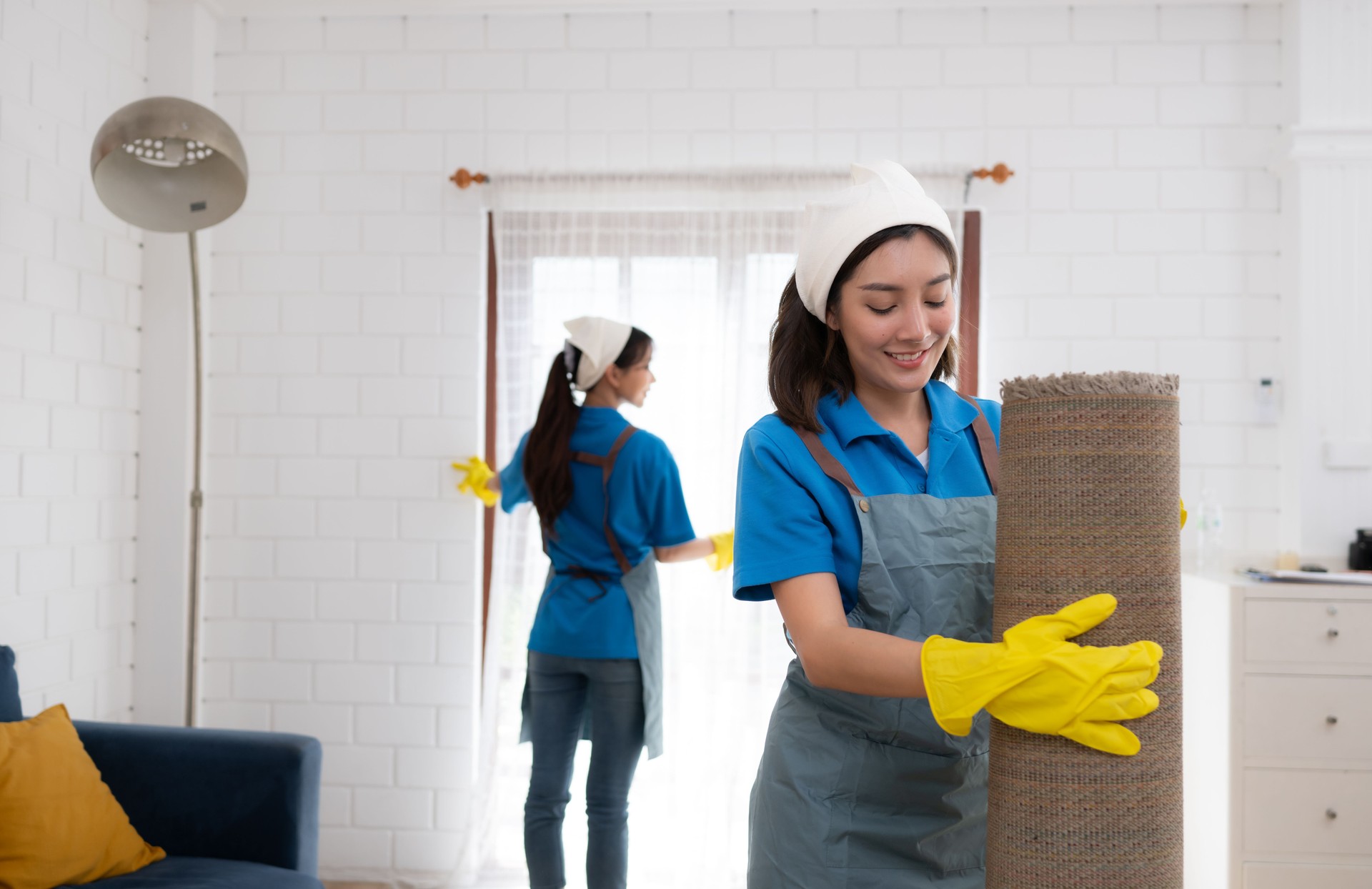 Young women cleaning maid in uniform and rubber gloves are cleaning the room, fold up carpet
